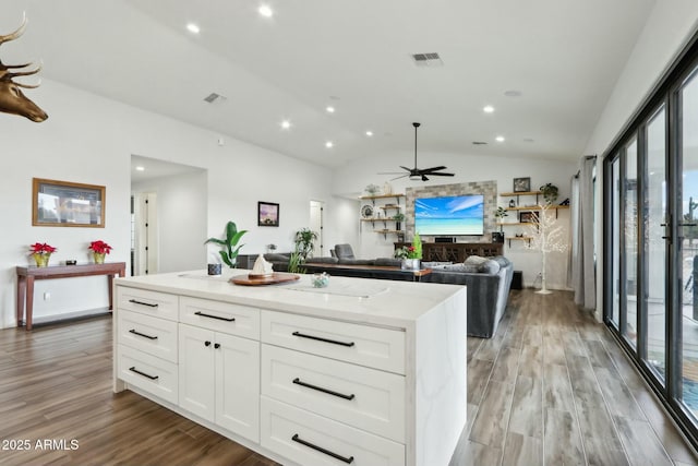 kitchen featuring vaulted ceiling, white cabinets, a center island, light stone counters, and light hardwood / wood-style floors