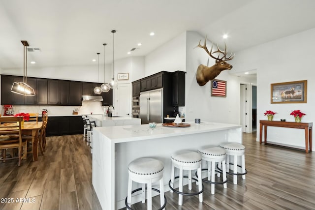 kitchen featuring pendant lighting, stainless steel built in refrigerator, sink, and a large island with sink