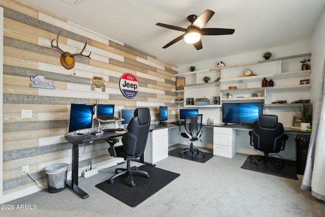 office area with built in desk, light colored carpet, ceiling fan, and wood walls