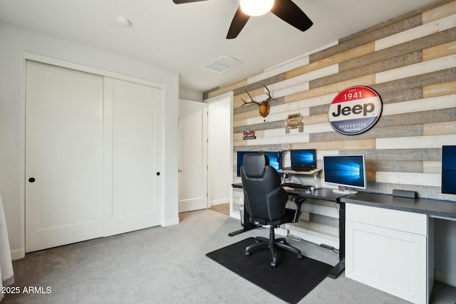 carpeted home office with ceiling fan, wooden walls, and built in desk