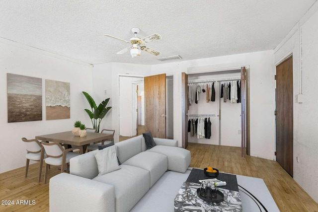 living room with a textured ceiling, light wood-type flooring, and ceiling fan