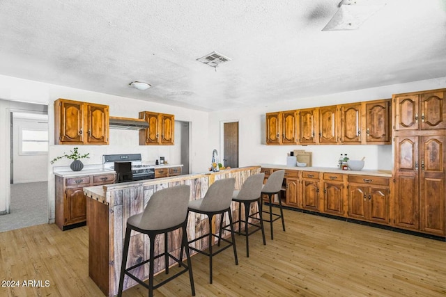 kitchen featuring black range with gas cooktop, a breakfast bar, exhaust hood, sink, and light hardwood / wood-style floors