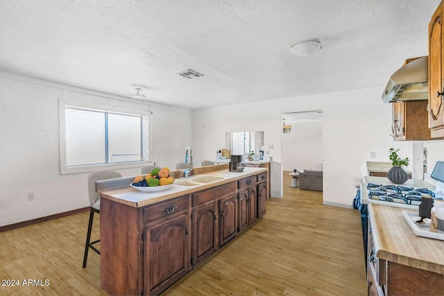 kitchen with white gas range oven, exhaust hood, a textured ceiling, and light hardwood / wood-style floors