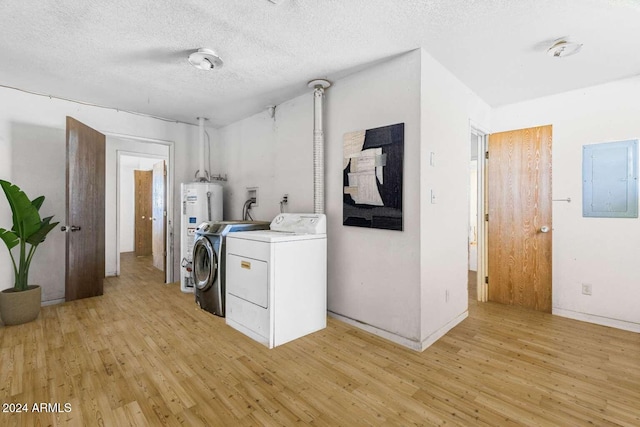 clothes washing area featuring electric panel, light hardwood / wood-style floors, water heater, and washing machine and clothes dryer