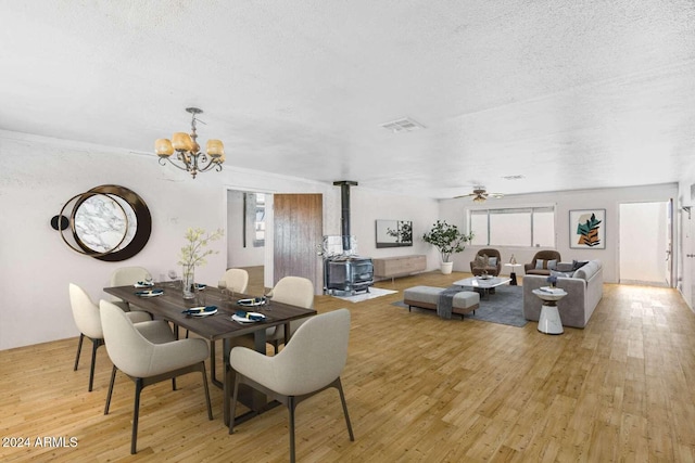 dining area featuring ceiling fan with notable chandelier, light hardwood / wood-style floors, a wood stove, and a textured ceiling