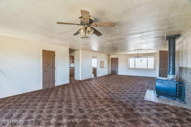 unfurnished living room featuring carpet flooring, a wood stove, ceiling fan, and a textured ceiling