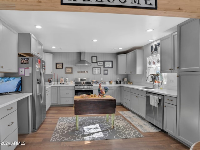 kitchen featuring gray cabinetry, stainless steel appliances, wood-type flooring, sink, and wall chimney range hood