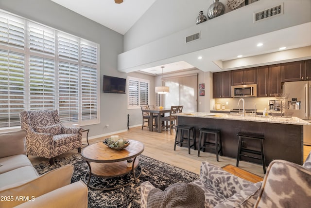 living room with plenty of natural light, sink, high vaulted ceiling, and light hardwood / wood-style flooring