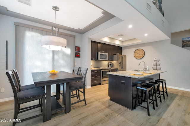 kitchen with dark brown cabinetry, a raised ceiling, a kitchen breakfast bar, a center island with sink, and appliances with stainless steel finishes