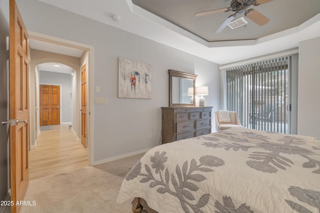 bedroom with light carpet, a raised ceiling, and ceiling fan