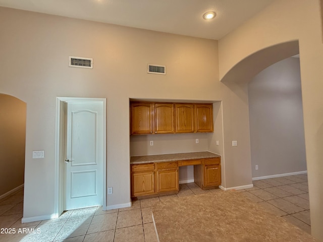 kitchen with light tile patterned flooring, visible vents, arched walkways, and built in desk