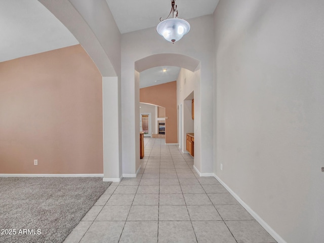 hall featuring arched walkways, light tile patterned floors, lofted ceiling, and baseboards