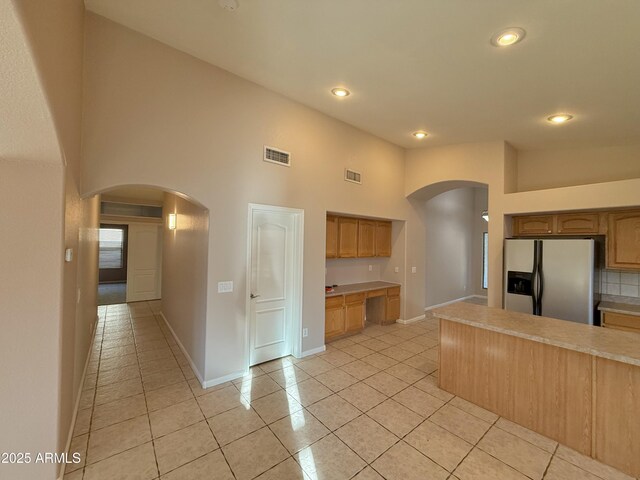 kitchen with arched walkways, visible vents, light countertops, and fridge with ice dispenser