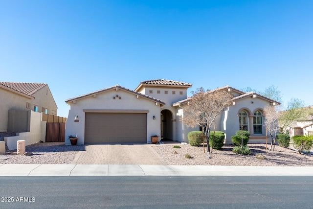 mediterranean / spanish home featuring fence, a tile roof, stucco siding, decorative driveway, and an attached garage