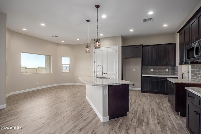 29785 N 203rd Dr, Wittmann, AZ 85361 - kitchen with a sink, stainless steel microwave, light stone countertops, light wood-style flooring, and backsplash