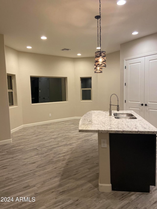 kitchen featuring a center island with sink, sink, light stone countertops, pendant lighting, and dark hardwood / wood-style flooring