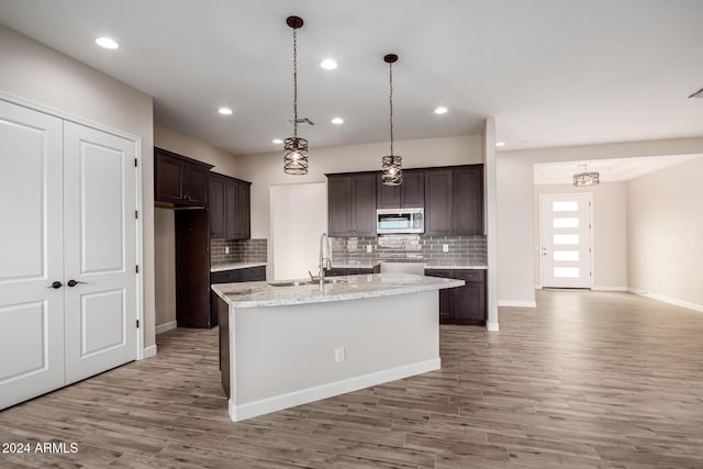 29785 N 203rd Dr, Wittmann, AZ 85361 - kitchen with stainless steel microwave, a sink, dark brown cabinetry, light wood-style floors, and decorative backsplash