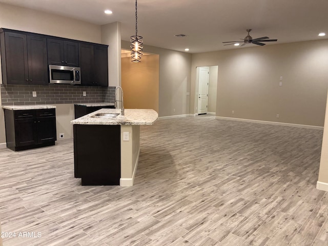 kitchen with decorative backsplash, sink, pendant lighting, light stone counters, and light hardwood / wood-style floors