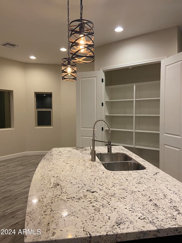 kitchen with an island with sink, light stone countertops, sink, and pendant lighting