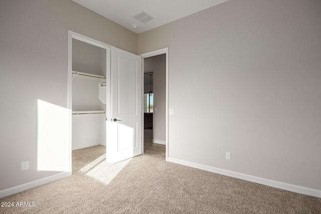 unfurnished bedroom with a spacious closet, light colored carpet, and a closet