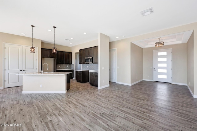 29785 N 203rd Dr, Wittmann, AZ 85361 - kitchen featuring stainless steel microwave, a kitchen island with sink, backsplash, dark brown cabinets, and open floor plan