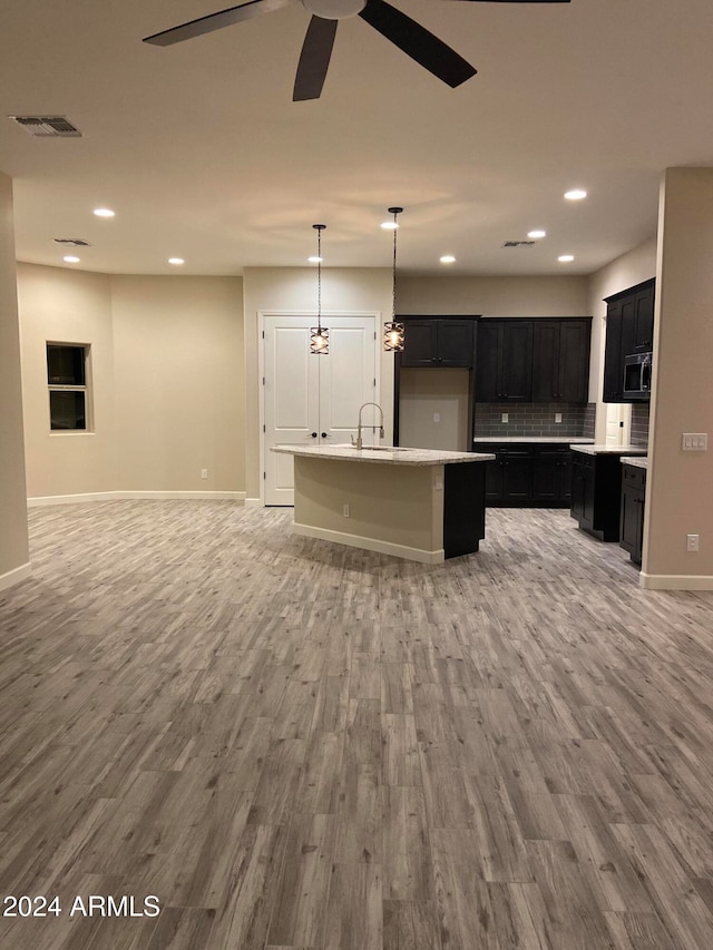 kitchen with ceiling fan, hanging light fixtures, light hardwood / wood-style flooring, and a kitchen island with sink