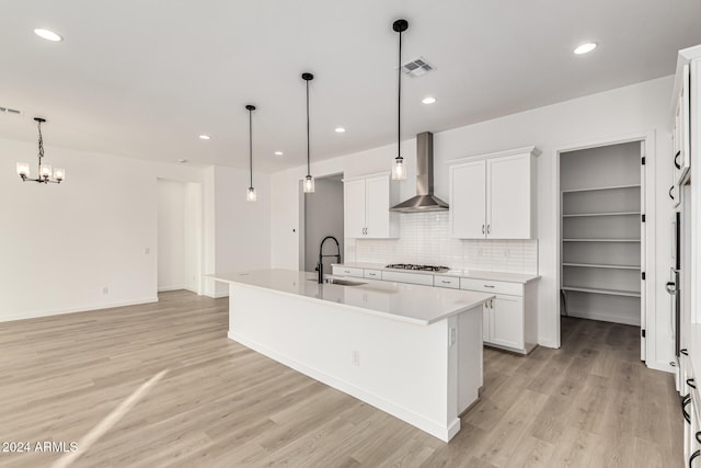 kitchen featuring decorative light fixtures, a center island with sink, wall chimney exhaust hood, and sink