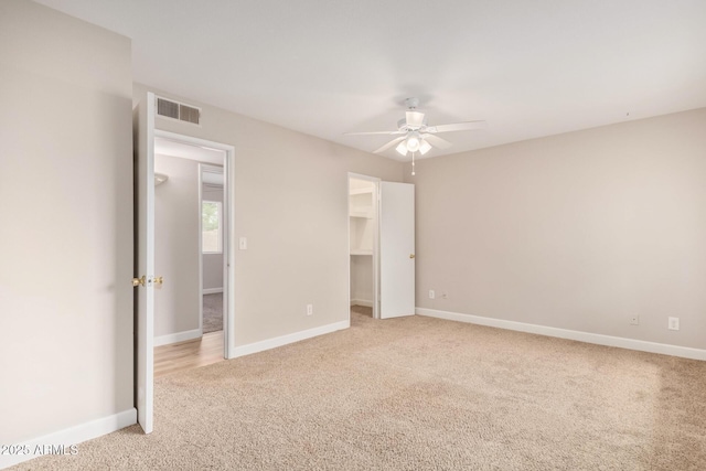 unfurnished bedroom with light carpet, a walk in closet, and ceiling fan