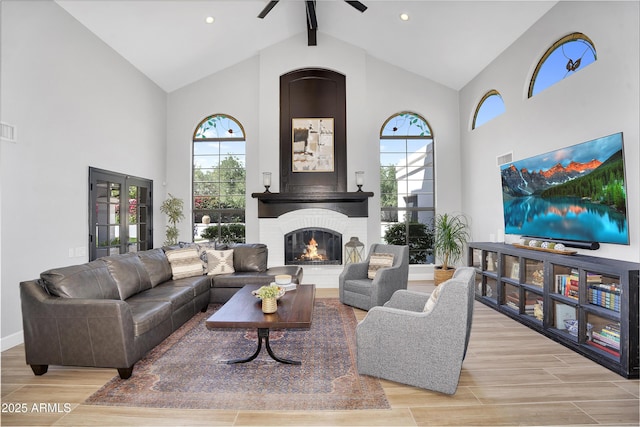 living area with high vaulted ceiling, ceiling fan, wood finish floors, a brick fireplace, and beam ceiling