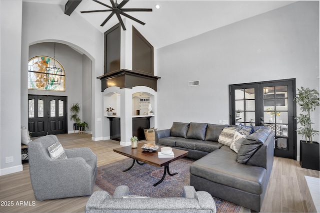 living area with french doors, a ceiling fan, light wood-style floors, visible vents, and high vaulted ceiling