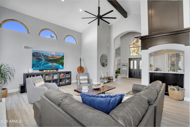 living area featuring a ceiling fan, visible vents, high vaulted ceiling, arched walkways, and light wood finished floors
