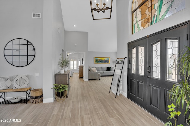 foyer featuring wood finished floors, a notable chandelier, visible vents, and a towering ceiling