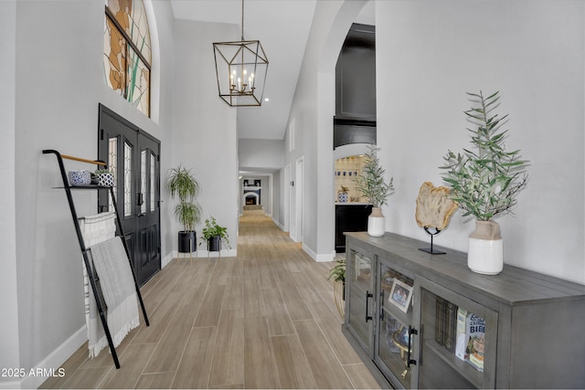 foyer featuring baseboards, arched walkways, an inviting chandelier, a high ceiling, and light wood-type flooring