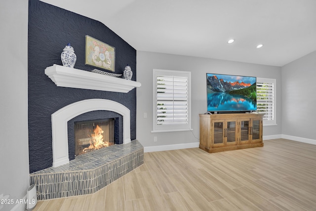 living area with a fireplace, baseboards, wood finished floors, and lofted ceiling