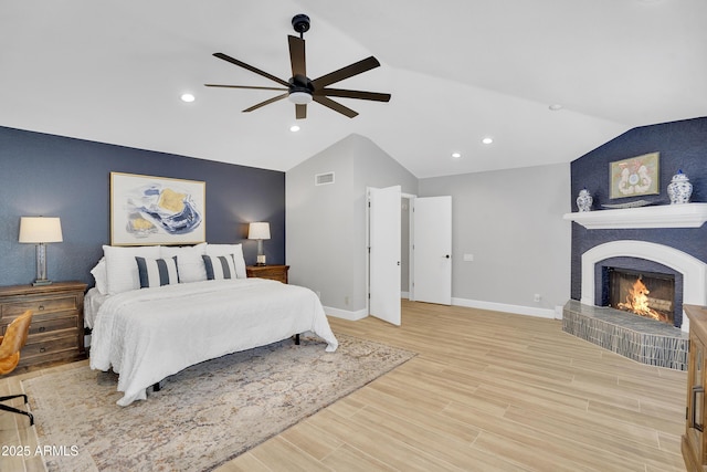 bedroom featuring visible vents, baseboards, a fireplace, light wood finished floors, and lofted ceiling