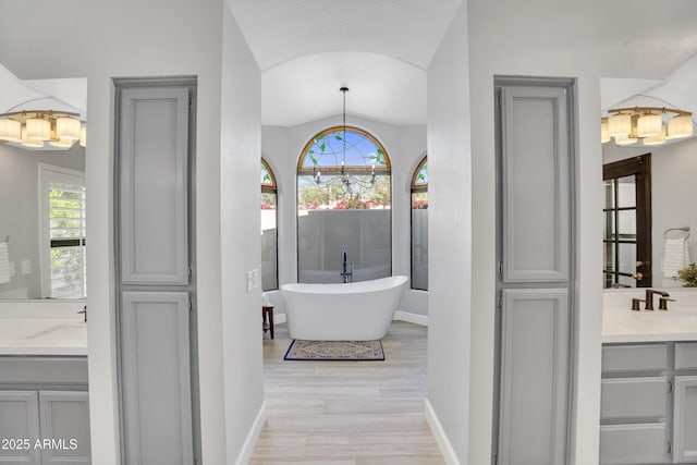 full bath featuring vanity, baseboards, a chandelier, a freestanding bath, and wood finished floors
