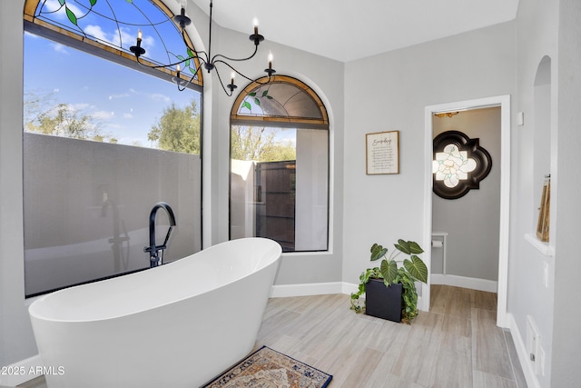 full bathroom featuring a chandelier, a freestanding tub, baseboards, and wood finished floors