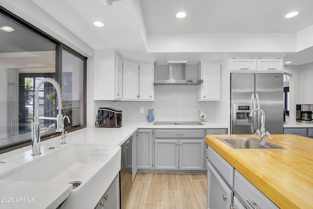 kitchen with a sink, stainless steel fridge with ice dispenser, wall chimney range hood, and black electric cooktop