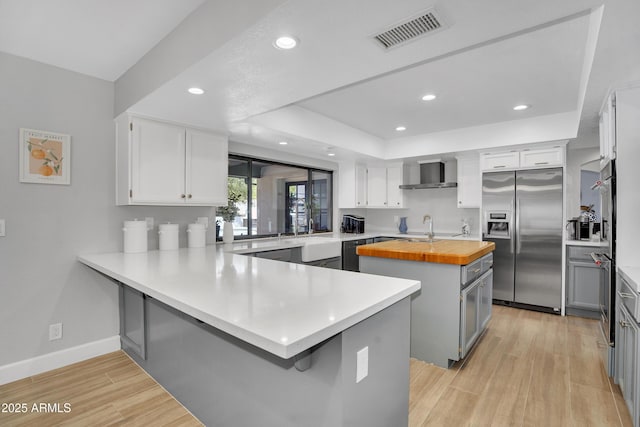 kitchen with wall chimney exhaust hood, visible vents, a kitchen island, appliances with stainless steel finishes, and butcher block countertops