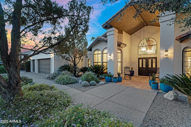 entrance to property with a tiled roof, stucco siding, french doors, a garage, and concrete driveway