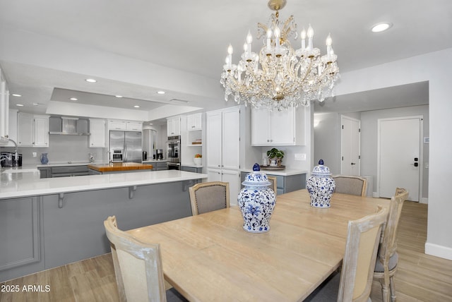 dining room with light wood-type flooring, baseboards, a chandelier, recessed lighting, and a raised ceiling