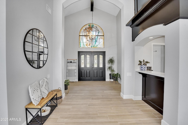 entryway featuring a notable chandelier, baseboards, a high ceiling, visible vents, and light wood finished floors