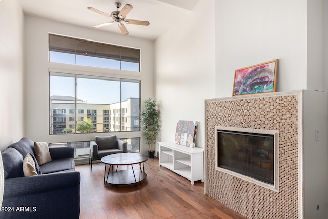 living room with a tile fireplace, ceiling fan, and dark wood-type flooring