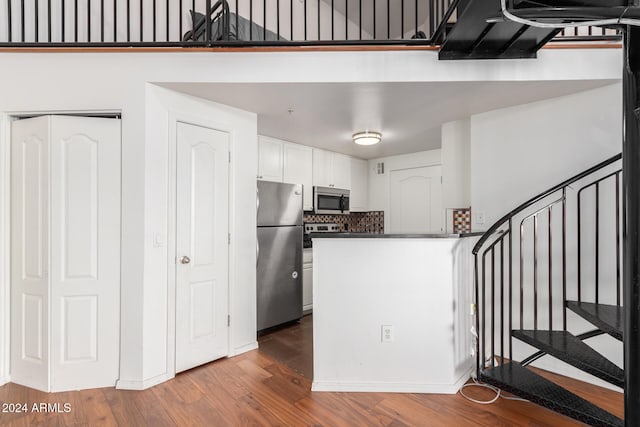 kitchen with kitchen peninsula, decorative backsplash, stainless steel appliances, wood-type flooring, and white cabinetry