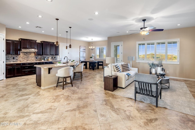 kitchen with a center island with sink, decorative light fixtures, a kitchen bar, light stone countertops, and ceiling fan with notable chandelier