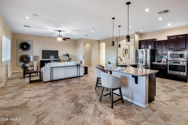 kitchen featuring sink, light stone counters, appliances with stainless steel finishes, a breakfast bar area, and decorative light fixtures