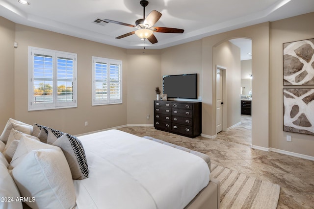 bedroom with ensuite bathroom, ceiling fan, and a raised ceiling