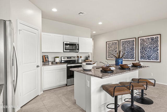 kitchen featuring stainless steel appliances, a kitchen bar, dark stone counters, light tile patterned floors, and a kitchen island with sink