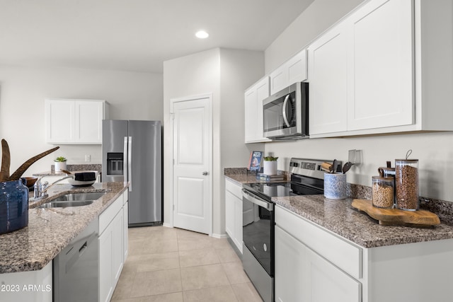 kitchen featuring appliances with stainless steel finishes, a sink, stone counters, white cabinets, and light tile patterned flooring