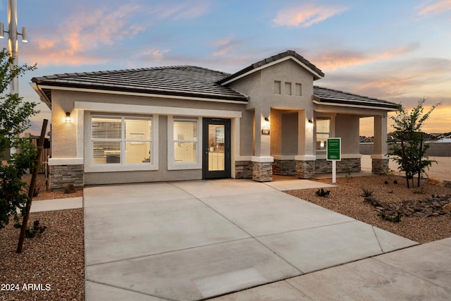 prairie-style house featuring stone siding, stucco siding, a tiled roof, and covered porch